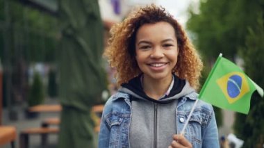 Gülümseyen ve Brezilya bayrağı ayakta dışında tutan kameraya, seyir Afrikalı-Amerikalı kadın mutlu turist Slowmotion portresi. Turizm ve insanlar kavramı.