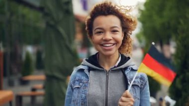 Kameraya bakarak, gülen ve Alman bayrağı açık havada tutan çekici Afrikalı-Amerikalı turist Almanya'da Slowmotion portresi. Turizm ve insanlar kavramı.