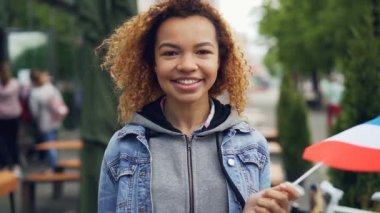 Slowmotion holding Fransız bayrağı ve yaz gününde kameraya bakarak gülümsemek güzel ve genç Afro-Amerikan kadın portresi. Mutlu turist ve millennials kavramı.