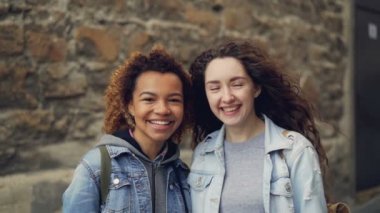 Yakın çekim slowmotion iki mutlu öğrenciler Afrikalı-Amerikalı ve kameraya bakıyor ve gülüyor Kafkas portresi. Karışık ırk dostluk ve şehir hayat kavramı.