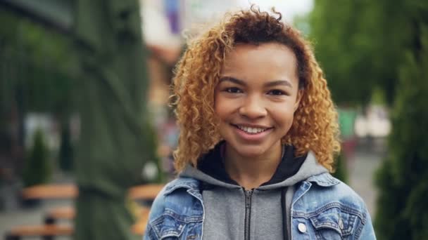 Portrait au ralenti d'un étudiant afro-américain regardant une caméra et souriant avec un beau parc vert en arrière-plan. Milléniaux, nature et concept de jeunesse heureuse . — Video