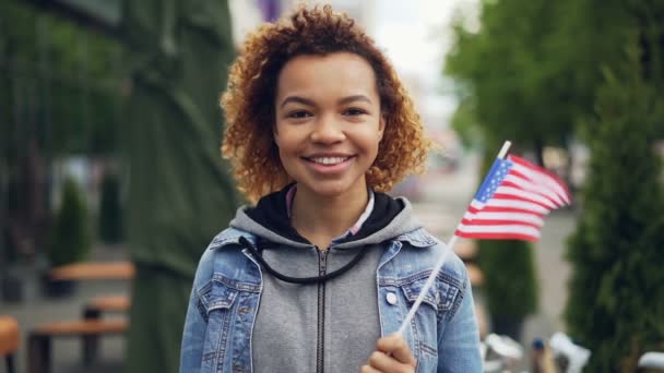 Lassú mozgás portréja csinos afroamerikai lány tinédzser látszó-on fényképezőgép, és gazdaság minket kívül álló modern város zászló. Turizmus, és az emberek koncepció. — Stock videók