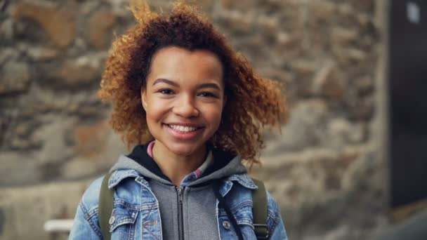 Close-up slowmotion portret van lachende Afro-Amerikaanse tiener in denim kleding kijken camera en poseren. Gelukkige jonge mensen en moderne levensstijl concept. — Stockvideo