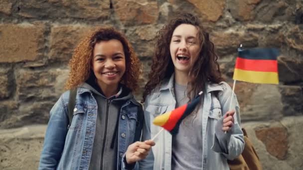 Slowmotion portret szczęśliwy studentów w Niemczech ładne dziewczyny macha niemieckiej flagi i śmiejąc się, patrząc na kamery. Przyjaźń, turystyka i koncepcja szczęśliwych ludzi. — Wideo stockowe