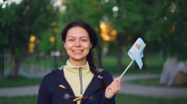 Genç Bayan Arjantinli fan Arjantinli dışında yeşil şehir parkında duran ve kameraya seyir ulusal bayrak sallayarak gülümseyen, ağır çekim portre.