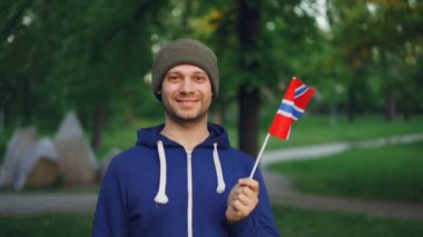 Ağır çekim portre yakışıklı Norveçli spor fan ulusal parkta duran ve gülümseyen Norveç bayrağı sallayarak. Kişi, aktif yaşam tarzı ve ülke kavramı.
