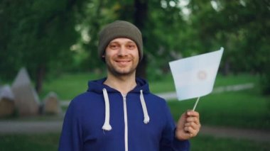 Ağır çekim Arjantinli kameraya bakarak ve gülümseyen ulusal bayrak sallayarak gurur Arjantinli vatandaş portresi. İnsanlar, milliyetçilik, modern toplum kavramı.