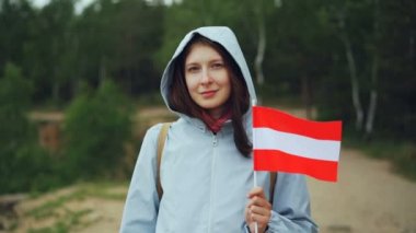 Ağır çekim gülümseyen ve kameraya bakarak Letonya, bayrağı tutarak oldukça Avusturyalı Bayan gurur vatandaş portresi. Milliyet, dünya ve insan kavramı seyahat.