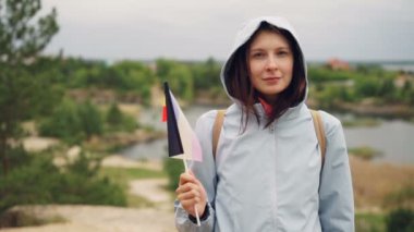 Ağır çekim portre Belçika resmi bayrağı tutarak ve güzel mutlu gülümseyerek kameraya bakarak neşeli turist. Ağaçlar ve göl güzel manzara arka planda olduğunu.