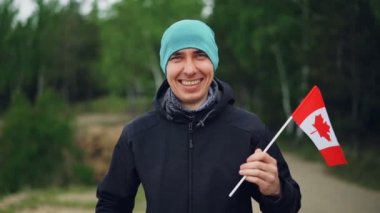 Ağır çekim portre gülümseyen ve güzel doğa yeşil ahşap arka plan ile kameraya bakarak Kanada bayrağı, holding mutlu dünya seyahati.