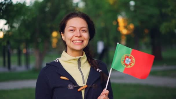 Portrait au ralenti de jolie Portugaise tenant le drapeau officiel du Portugal, souriant et regardant la caméra. Concept de femmes actives, fans de sport, pays et personnes . — Video