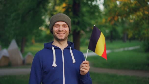 Slow motion porträtt av belgiska man i sport jacka och mössa holding Belgien flagga med lyckligt leende och tittar på kameran. Personer och nationalitet koncept. — Stockvideo