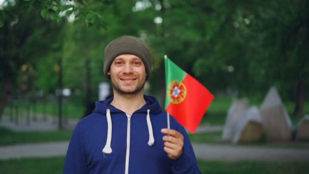 Retrato en cámara lenta del atractivo deportista portugués ondeando la bandera de Portugal, sonriendo y mirando a la cámara. Ciudadanos, orgullo nacional, concepto de estilo de vida activo . — Vídeos de Stock