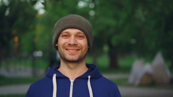 Close-up slowmotion portret van gelukkig sportman glimlachen en kijken naar camera staande in park in het voorjaar. Actieve levensstijl, gezonde mensen en geluk concept. — Stockvideo
