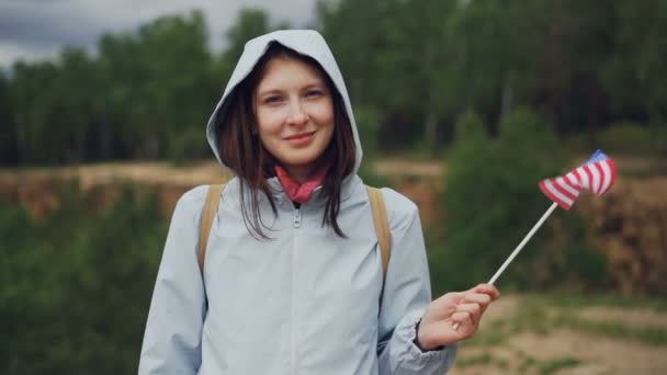 Повільний рух портрет досить американської жінкою, розмахуючи прапором Сполучених Штатів з щасливою усмішкою і дивлячись на камеру. День незалежності і концепція народу. — стокове відео