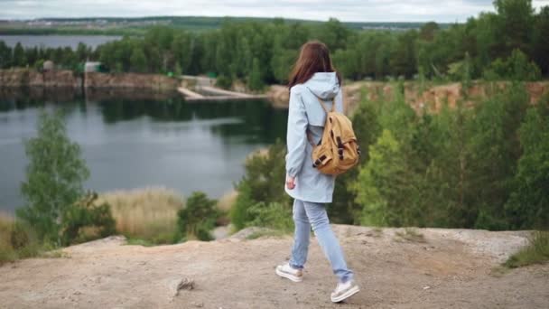 Retrato em câmera lenta de uma jovem ruiva caminhando até a beira do penhasco e observando uma vista emocionante de lagos, bosques e edifícios. Belo conceito de natureza e turismo . — Vídeo de Stock