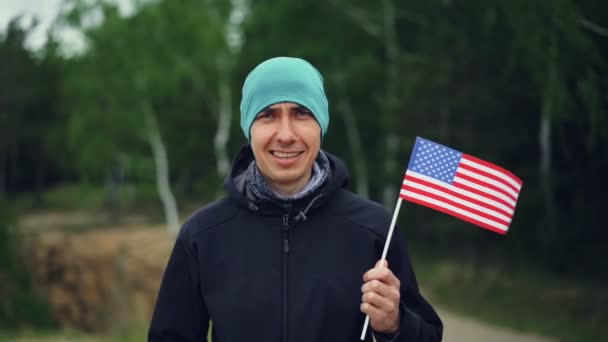 Retrato em câmera lenta de cara bonito cidadão americano segurando bandeira dos Estados Unidos, sorrindo e olhando para a câmera. Conceito de cidadania, pessoas e países . — Vídeo de Stock