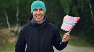 Ağır çekim portre resmi ormanda ayakta ve gülümseyen Norveç bayrağı sallayarak yakışıklı Norveçli spor fan. İnsanlar, Milliyet ve ülke kavramı.