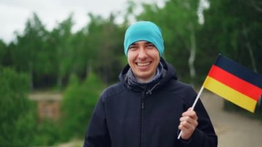 Yavaş hareket portraif bir Alman bayrağı sallayarak, gülen ve kameraya bakarak mutlu göçmen yakışıklı adam. Dünya seyahat, heyecanlı insanlar ve ülkeler kavramı.