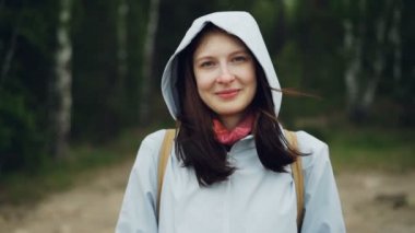 Ağır çekim gülümseyen ve arka planda yüksek yeşil ağaçlar ile kamera ayakta ormandaki bakarak çekici genç kadın portresi. Doğa ve insan kavramı.