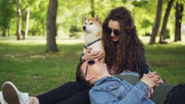 Çekici gülümseyen kadın onunla konuştuğunu ve iyi yetişmiş köpeği okşama neşeli genç adam parkta çim kafasıyla hanımları bacaklarına yalan söylüyor.