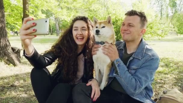 誇りに思って犬所有者幸せなカップルは、美しいペットと楽しいスマート フォンを見てそれを騒ぐと selfie を取っています。現代のライフ スタイル、動物、技術の概念. — ストック動画