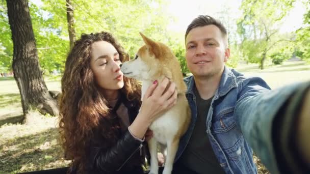 Punto de vista de la toma de fotos de pareja casada selfie con mascota shiba inu perro, los jóvenes están hablando, riendo y acariciando al animal mientras mira a la cámara . — Vídeos de Stock