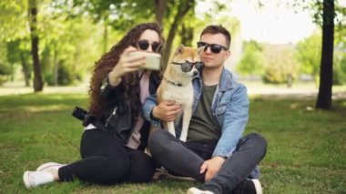 Güzel kadın selfie onun erkek arkadaşı ve sevimli köpek parkta çim üzerinde dinlenme süre smartphone kullanarak alıyor. İnsan ve hayvanların güneş gözlüğü takıyor.