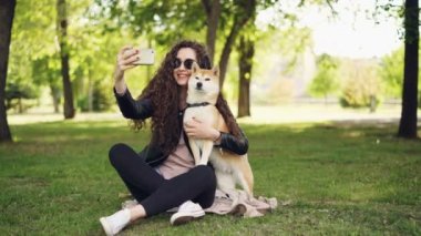 Neşeli blogger evde beslenen hayvan sahip selfie smartphone, kullanarak onu köpek ile insan ve hayvan Park'ın bahçesinde oturup ve alıyor poz, kadın sevecen ve köpek öpüşme.