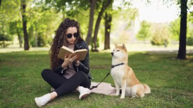 Çekici genç kadın iyi yetişmiş köpeğini onu sahip oturuyor iken Park çimenlerin üzerinde oturan ve etrafa kitap okuyor. Eğlence ve hayvanlar kavramı.