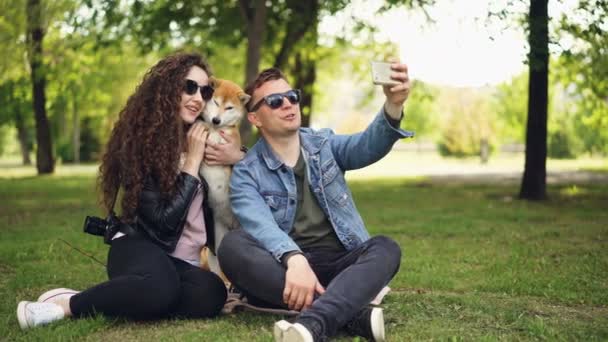 Popular blogger está grabando vídeo sobre sí mismo, su esposa y lindo perro, el hombre está sosteniendo el teléfono inteligente, hablando y mirando a la cámara a continuación, en la mujer y el animal . — Vídeos de Stock