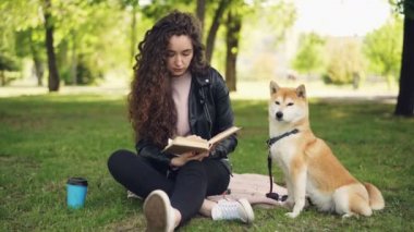 Genç ve güzel kadın parkta kitap okuyor ve sevimli köpek shiba Inu doğurmak okşamaya, iyi yetişmiş evde beslenen hayvan sahibi yakınındaki çimlerde oturuyor. Hayvanlar ve insanlar kavramı.