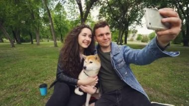 Neşeli adam akıllı telefon tutarak ve sevimli köpek tutarken eşi öpüşme ve o öpüşme selfie alıyor. İlişki, aşk, romantizm ve modern teknoloji kavramı.