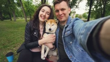 Bakış açısı shot iki mutlu insanlar ve selfie Parkı, Öpüşme ve sevgi ve bakım ifade sevgi dolu alarak köpek yavrusu. Güzel yeşil çim ve ağaç arka planda vardır.