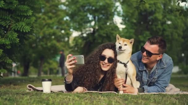 Giovane Donna Sta Prendendo Selfie Nel Parco Che Si Trova Sullerba Con Il Suo Ragazzo E Il Cane Adorabile Animale Sta Starnutendo E Leccare Il Suo Naso Persone Stanno Ridendo