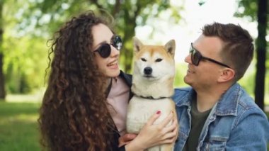 Yavaş hareket iki kişi bakım köpek pet öpüşme ve çok güzel safkan okşamaya sahipleri şehir parkında çimenlerin üzerinde oturma. Aşk, ilişki ve doğa kavramı.