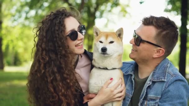 Slow motion van twee mensen zorgzame hond huisdier eigenaren kussen en klopte schattig stamboom zittend op het gras in park in de stad. Liefde, relatie en natuur concept. — Stockvideo