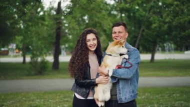 Ağır çekim portre sevimli köpek yavrusu holding, kameraya bakıyor ve ayakta Park yaz gününde gülümseyen erkek ve kadın gurur köpek sahiplerinin.