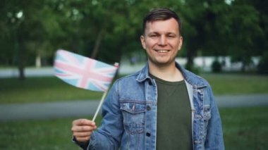 Gülümseyen ve Birleşik Krallık resmi bayrak sallayarak kameraya, seyir neşeli İngiliz ağır çekim portre. Dünya ve insanlar kavramı seyahat.