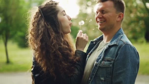 Zpomalený pohyb rozkošný pár bavit v parku, mladá žena fouká Pampeliška blowball v její tváři milenci, on se směje a zavřel oči. — Stock video