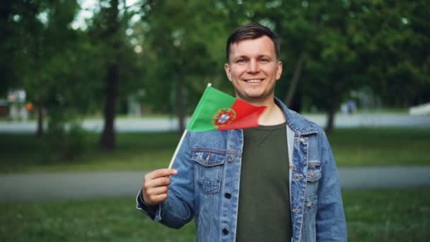 Zpomalený pohyb portrét pohledný muž v neformálním oblečení mává Portugalská vlajka se šťastným úsměvem a při pohledu na fotoaparát. Sportovní fanoušci, cestující a vlastenci koncepce. — Stock video