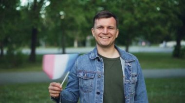 Ağır çekim kamera güzel yeşil şehir park dururken bakarak mutlu gülümseme ile Fransız bayrağı sallayarak yakışıklı Fransız gurur vatansever portresi.