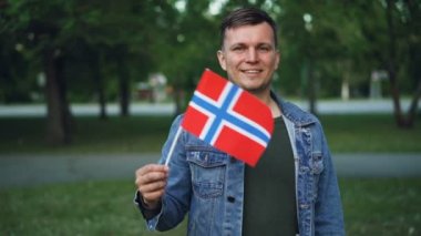 Ağır çekim portre Norveçli spor fan açık havada duran ve kameraya bakarak gülen Norveç bayrağı sallayarak. Milli takım ve ülke kavramı destekleyen.
