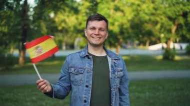 Ağır çekim portre etkileyici yüz İspanyol resmi bayrağı sallayarak yakışıklı genç adam gülümseyen ve kameraya bakıyor. Mutlu insanlar ve ulusal gurur kavramı.