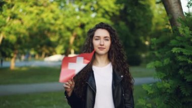 Ağır çekim portre çekici genç kadın gurur İsviçre vatandaşı İsviçre'nin ulusal bayrak sallayarak, kameraya bakıyor ve gülümsüyor. Ülkeler ve milletlerden kavramı.