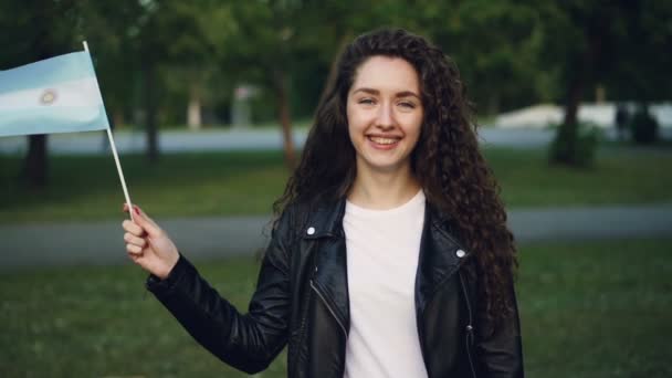 Portrait au ralenti d'une femme argentine attirante agitant le drapeau officiel de l'Argentine, regardant la caméra et riant. Milléniaux, peuple et concept de nationalisme . — Video