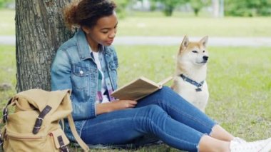 Oldukça Afrika kökenli Amerikalı öğrenci okuma kitabı ile itaatkar onun köpek çimlerin üzerine oturan Park portresi. Modern yaşam tarzı, doğayı ve hayvanları kavramı.