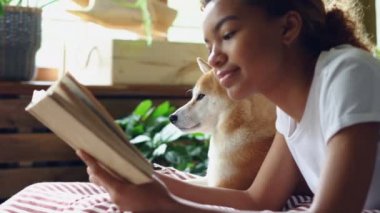 Çok güzel itaatkar pet yakınındaki modern düz yatakta yatarken kitap okuma karışık yarış kız köpek sahibi yakın çekim shot. İlginç hobi, edebiyat ve hayvanlar kavramı.