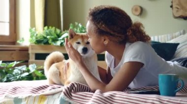 Mutlu kız öğrenci onu küçük köpek besleme ve bu süre hayvan çiğneme, onun ağız ve burun yalama ve lezzetli yemekler ve sevgi zevk evde, yatakta yatarken okşama.