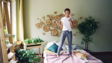 Güzel genç bayan kulaklık ile müzik dinlemek ve evde yatakta onun yanında oturan sevimli shiba Inu köpek dans smartphone kullanarak.